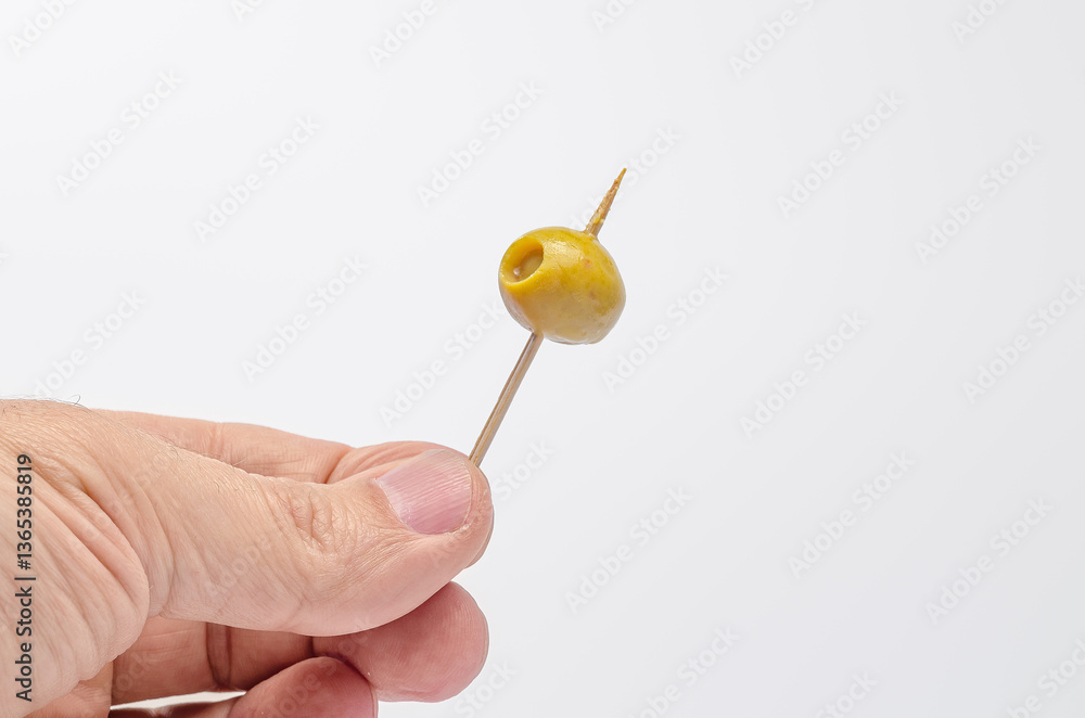 Hand presenting a green olive on a toothpick for a mediterranean appetizer Hand presenting a green olive on a toothpick for a mediterranean appetizer