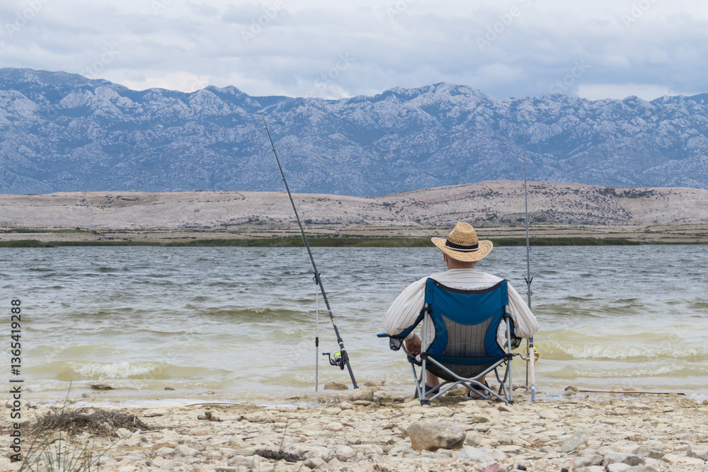 Rear view of old unrecognizable fisherman wearing a straw hat, sitting in fishing chair with two fishing poles. Rear view of old unrecognizable fisherman wearing a straw hat, sitting in fishing chair with two fishing poles.