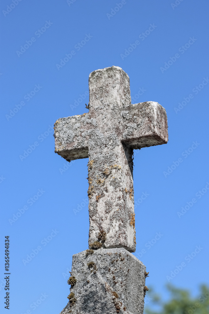 Old stone cross on grave. The sky is blue and cloudless. There is lichen and moss on the surface of the cross. Old stone cross on grave. The sky is blue and cloudless. There is lichen and moss on the surface of the cross.
