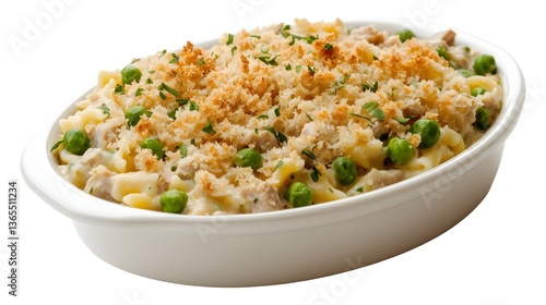 Baked tuna noodle casserole topped with golden breadcrumbs and green peas. Creamy pasta dish served in a white oval dish on a white background.