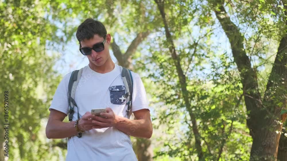 A tourist in sunglasses and a backpack stands among the trees, scrolling through photos on phone from his walk. He lingers on each shot, immersed in the memories of the landscapes captured. A tourist in sunglasses and a backpack stands among the trees, scrolling through photos on phone from his walk. He lingers on each shot, immersed in the memories of the landscapes captured.