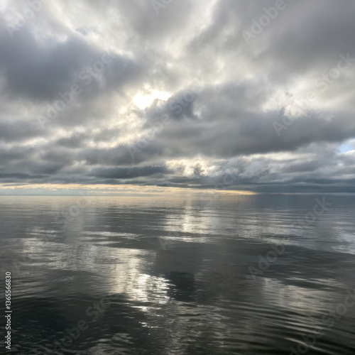 calm sea beneath gray overcast sky reflects soft light, creating serene and tranquil atmosphere