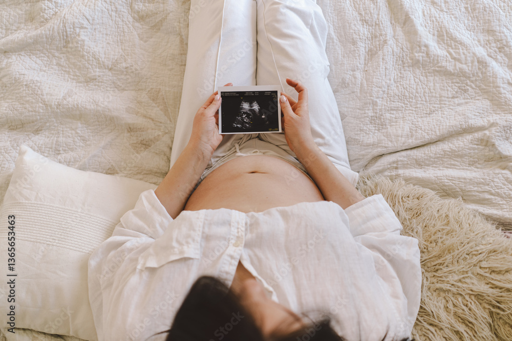 A Woman cradles an ultrasound image against their pregnant belly while capturing a moment of anticipation and connection at home. A Woman cradles an ultrasound image against their pregnant belly while capturing a moment of anticipation and connection at home.