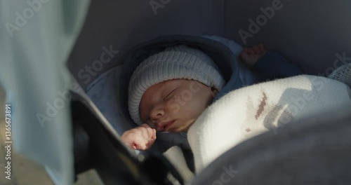 Close-up portrait of a newborn baby boy in a hat sleeping in a stroller covered with blanket.