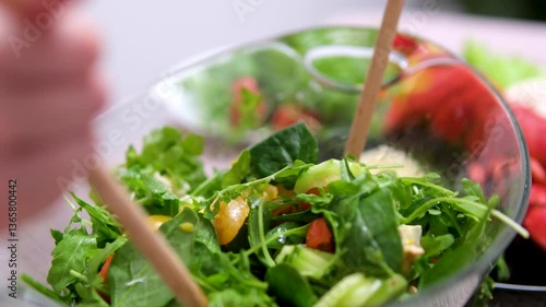 Fresh salad with lettuce leaves and tomato falling into bowl, served with healthy food ingredients on white table, slow motion