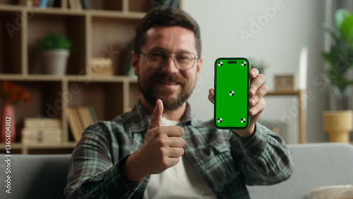 Fotografie Caucasian man male guy smiling showing green screen smartphone display app at ho
