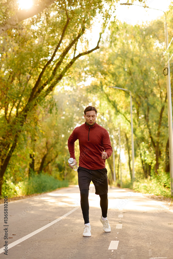 Obraz premium Stylish young man jogging in a sunlit pathway surrounded by vibrant autumn trees