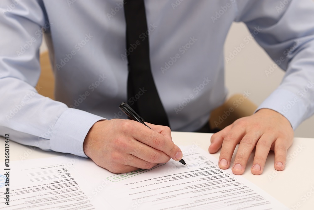Man signing licensing agreement document at white table indoors, closeup