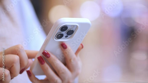 Woman is holding a white iPhone with a red nail polish on her nails. She is texting on the phone