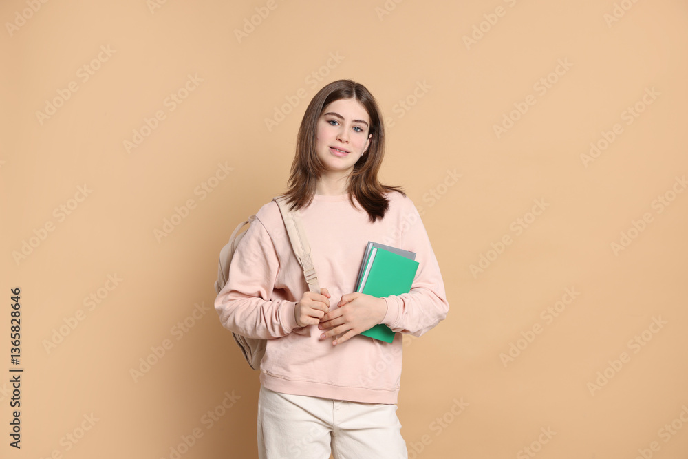 Fototapeta premium Portrait of teenage girl with books and backpack on beige background