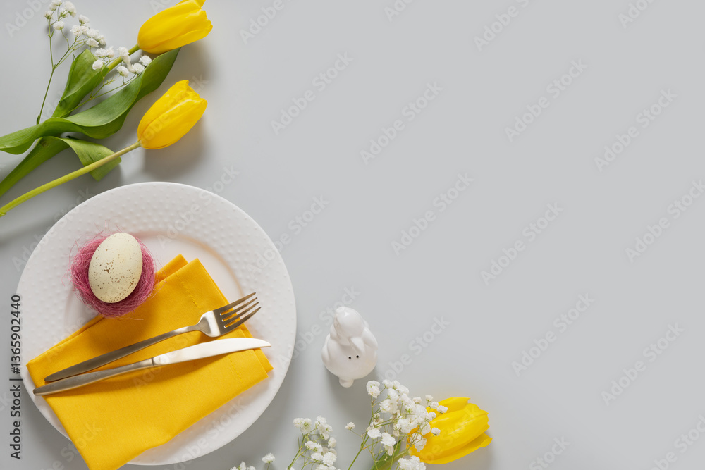 Spring Easter table setting with yellow tulips, white plate, bunny, eggs on gray background. Happy Easter celebration. Copy space. View from above.