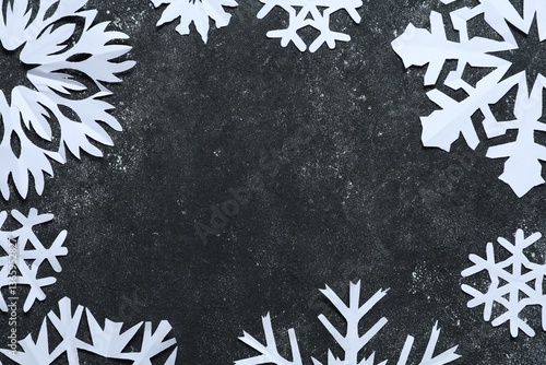 Frame of beautiful paper snowflakes on dark grey table, flat lay. Space for text