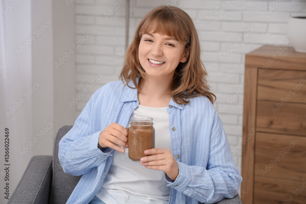 Happy young woman with jar mug of tasty iced latte sitting on armchair at home Happy young woman with jar mug of tasty iced latte sitting on armchair at home