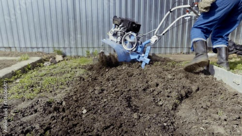 Man uses tiller to prepare backyard soil for planting Agriculturalist actively plowing field with tiller outdoors