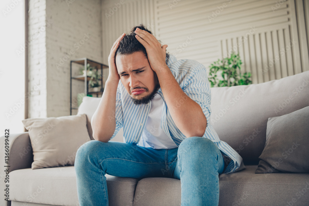 Obraz premium Young man showing stressed emotions while sitting on a couch in a bright and stylish living room interior