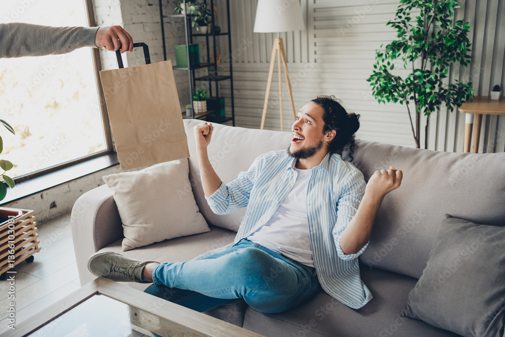 Fototapeta premium Young man relaxing on couch receives delivery, excited in bright living room