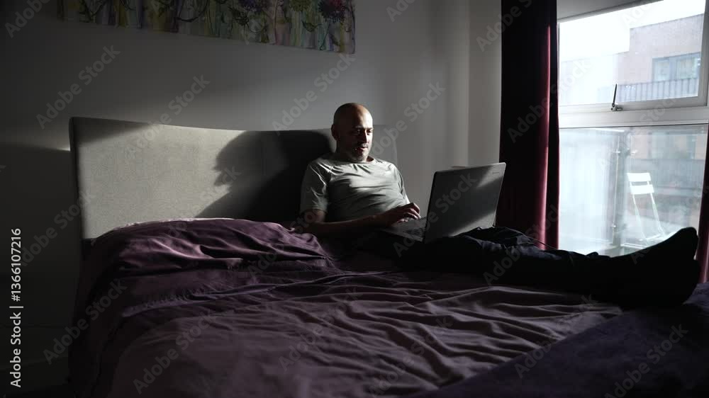 South asian man working from home, using laptop in bed, taking advantage of morning light South asian man working from home, using laptop in bed, taking advantage of morning light