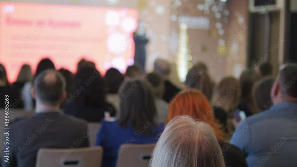 Group of people are sitting in a room and looking at a screen. The screen has a red background and the words Group of people are sitting in a room and looking at a screen. The screen has a red background and the words