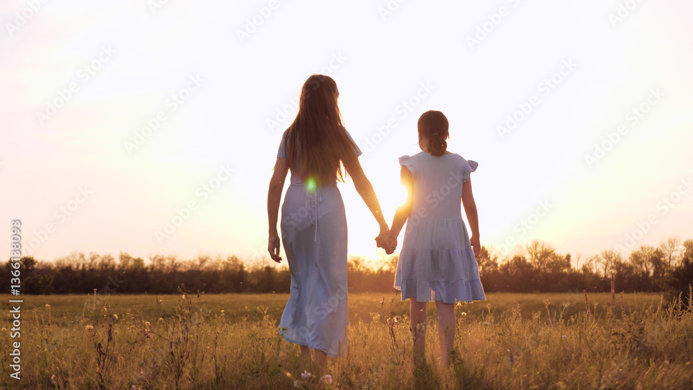 Happy mother and daughter go into the sunset. A woman dressed in a dress holds the hand of a little girl daughter. A schoolgirl holds her mother's hand. Childhood love for mother. Happy family Happy mother and daughter go into the sunset. A woman dressed in a dress holds the hand of a little girl daughter. A schoolgirl holds her mother's hand. Childhood love for mother. Happy family