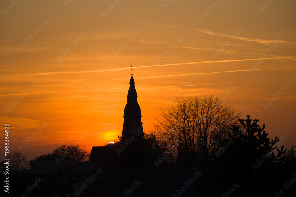 Obraz premium Sunset at the golden hour with the silhouette of the Christuskirche and a leafless tree in Ratingen Homberg with orange sky 