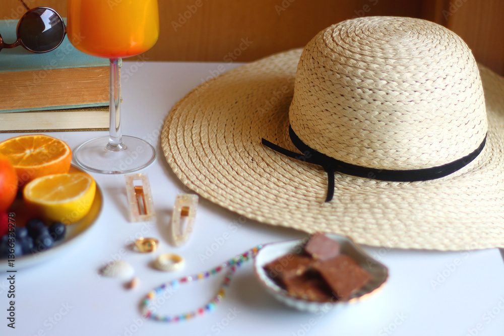 Glass of cocktail, straw hat, sunglasses, books, fresh fruit, chocolate and accessories. Summer essentials on the table. Selective focus.
