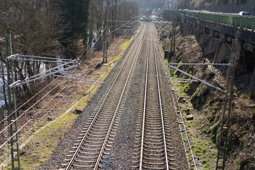 A close-up train tracks with power lines next to a stone wall. Railway transportation concept