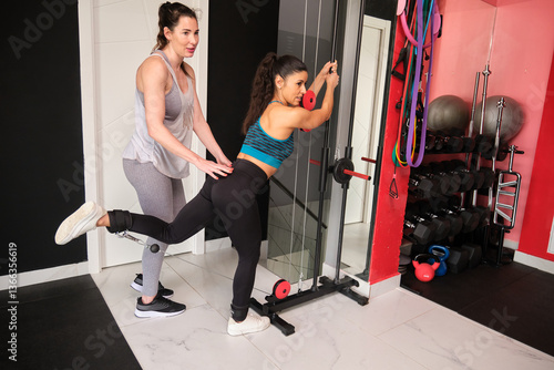 Obraz na płótnie Woman using cable machine with personal trainer assisting in modern gym w salonie