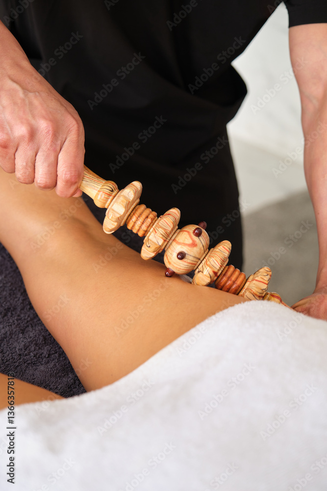 Therapist using wooden roller tool during leg massage treatment