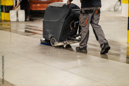 Unrecognizable worker washing garage floor with scrubber machine.