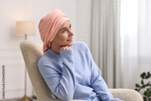 Smiling woman with cancer in headscarf on armchair indoors