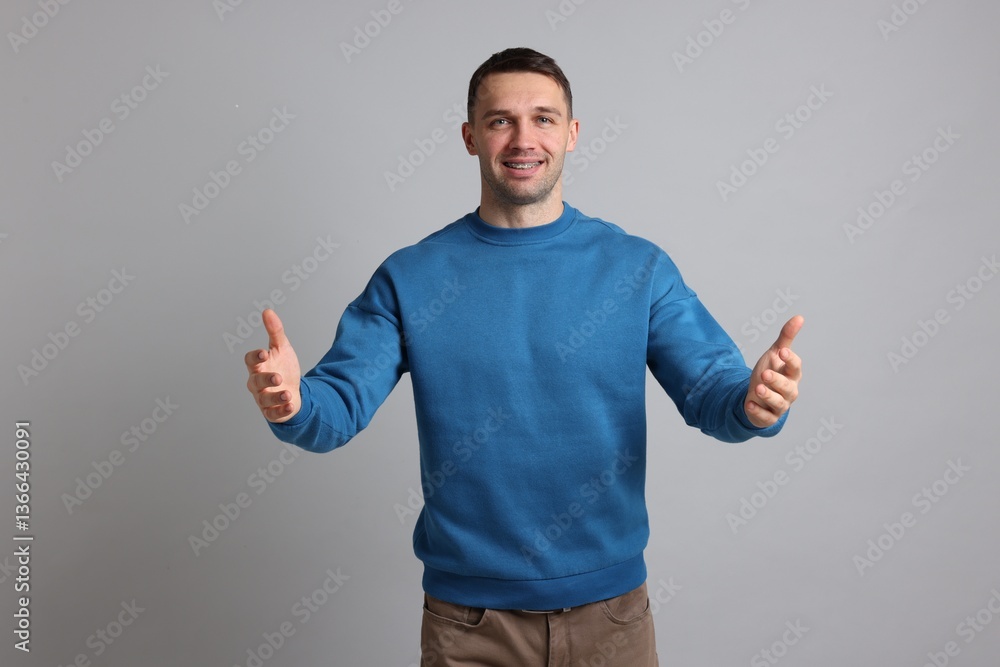 Cheerful man welcoming guests on light grey background Cheerful man welcoming guests on light grey background