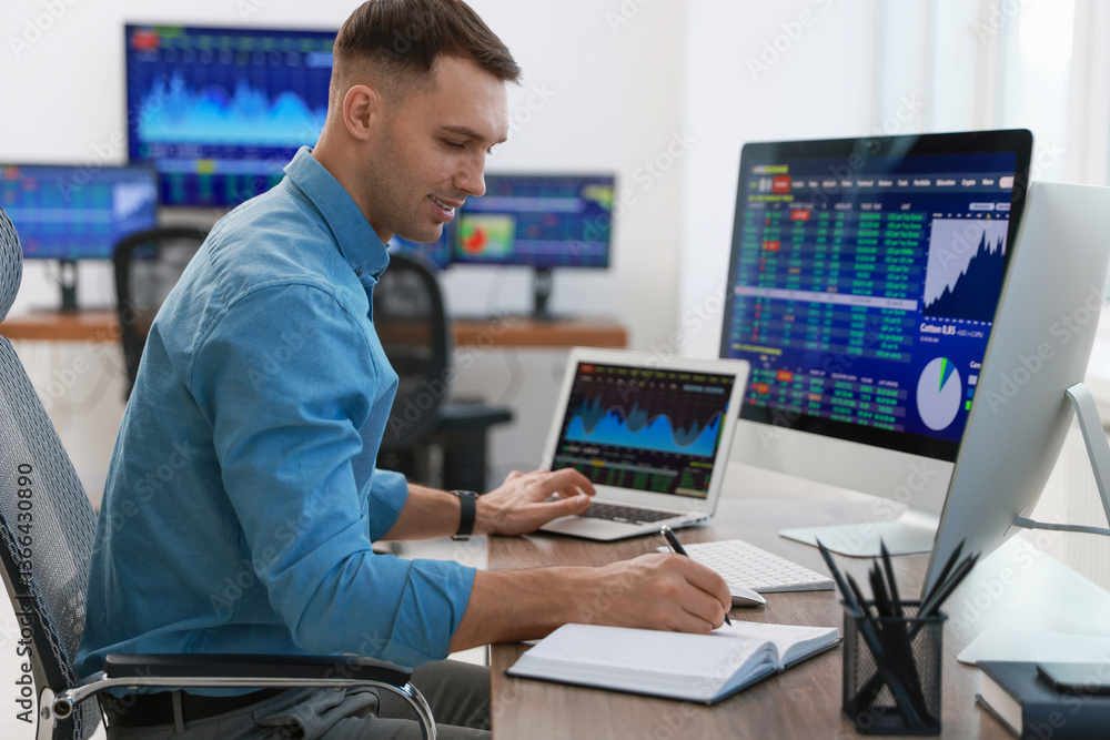 Financial trading specialist writing notes at table in office Financial trading specialist writing notes at table in office