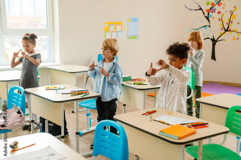 Obraz premium Four children, including a Black girl, Caucasian boy, multiracial boy, and red-haired Caucasian girl, learning sign language in a classroom. They are standing near desks with school supplies.