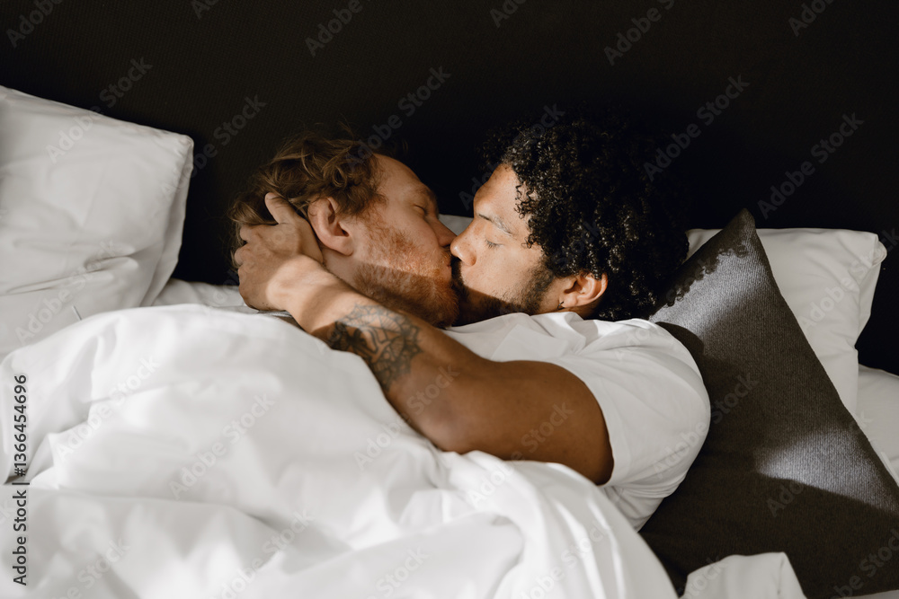 Fototapeta premium Gay couple, a man lies in bed and holds the head of the man lying next to him, they kiss with closed eyes, in the bedroom