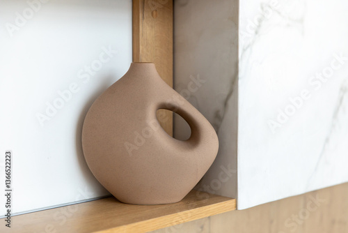 A modern matte curved shaped ceramic vase with an unusual wavy brown shape on the shelf.