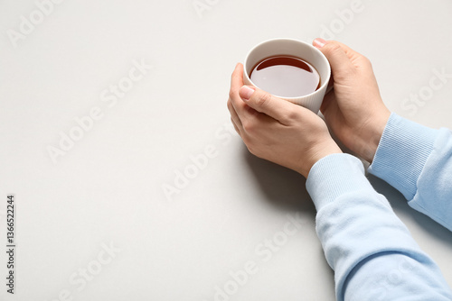 Female hands holding cup of black tea on light background