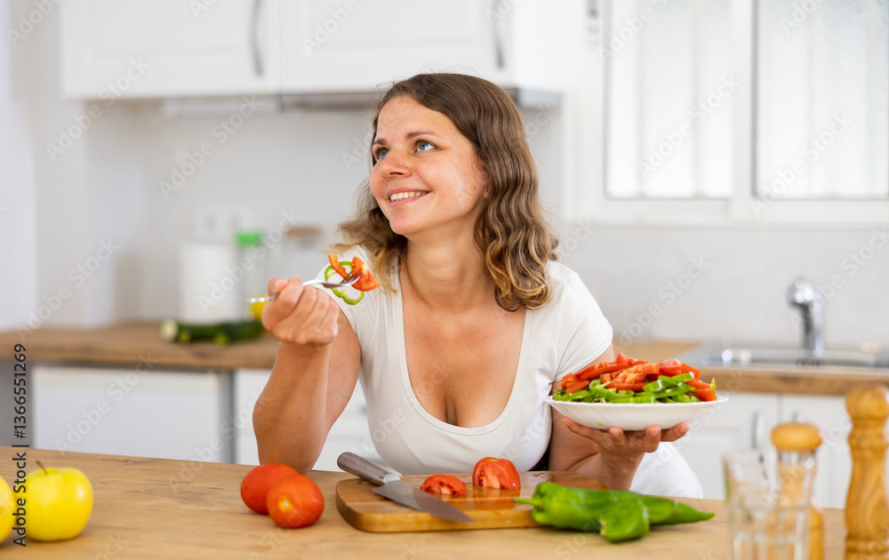 Young smiling woman tasting healthy vegetable salad at kitchen Young smiling woman tasting healthy vegetable salad at kitchen