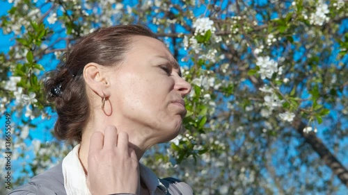 Scratching neck during allergy. A view of stressed female scratching her skin because of pollen allergy during spring promenade in the park.
