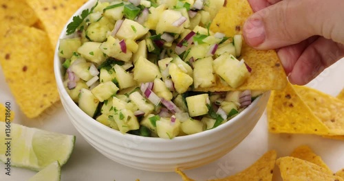 Pineapple salsa in a bowl served with chips, scooping salsa with a chip