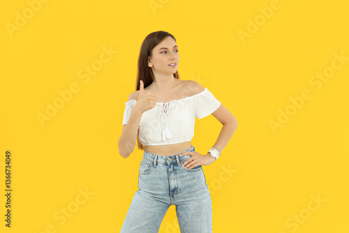 Attractive young girl on yellow background shows thumb up