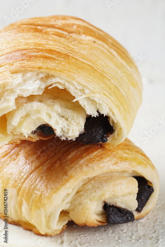 A single pain au chocolate pastry placed on a white textured surface, showcasing its golden, flaky layers and rich chocolate filling.