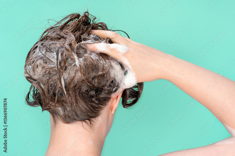 Naklejka premium A woman washes her hair with shampoo on mint background, rear view.
