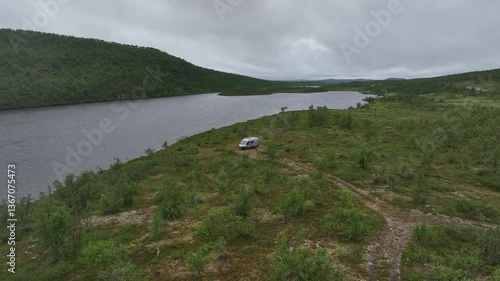 Drone view of a van in the vast green landscape of Masi,  Norway, near calm waters