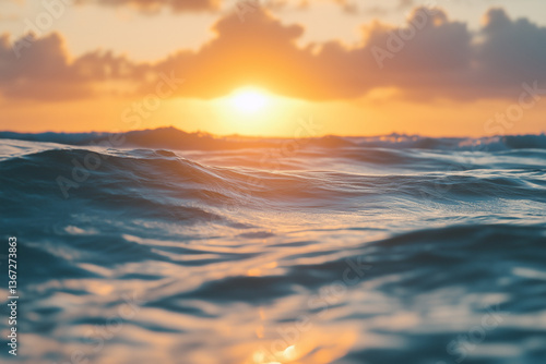 A vast ocean with gentle waves rolling across the surface, reflecting the golden light of a setting sun. The perspective is close to the water level, capturing the rich texture of the waves.