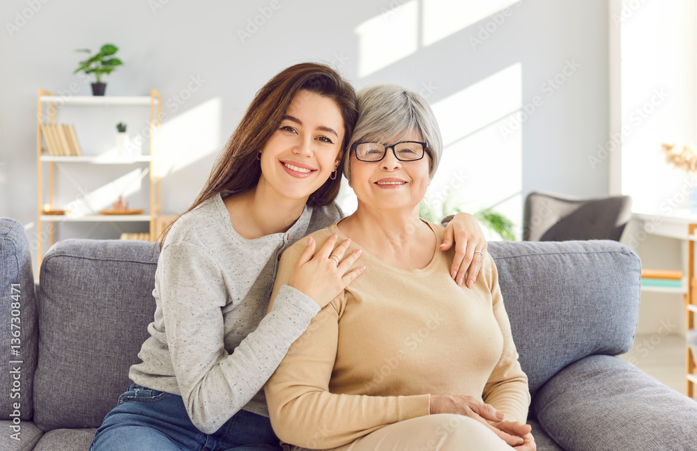 Portrait of a happy smiling adult daughter hugging her senior gray-haired old mother parent resting on couch at home and looking cheerful at camera. Love, family and Mothers day concept. Portrait of a happy smiling adult daughter hugging her senior gray-haired old mother parent resting on couch at home and looking cheerful at camera. Love, family and Mothers day concept.