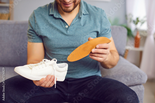 Fotografie Man is sitting on the sofa, inserting an orthopedic insole into his shoe