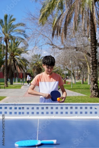 education, children and sports concept. ping pong. preteen boy playing ping pong in a park.