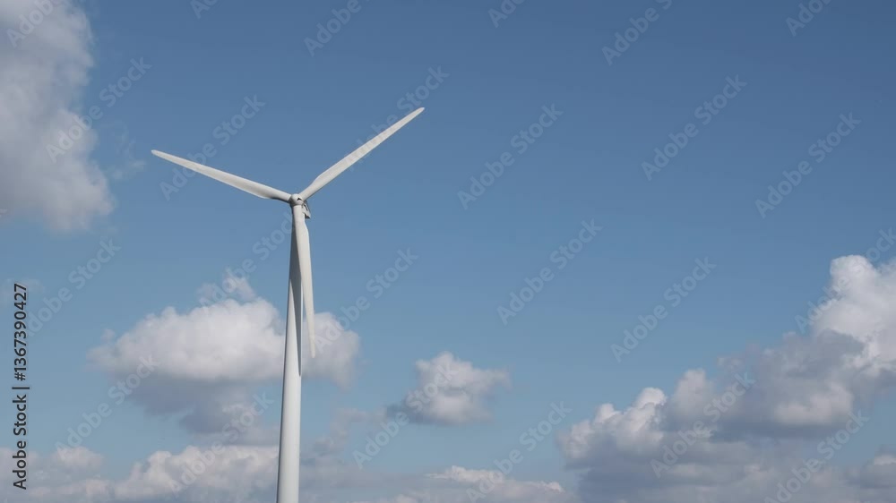 A wind generator rotates against a cloudy blue sky and produces electricity. Green energy concept, which is generated from natural resources such as wind, sun, water. A wind generator rotates against a cloudy blue sky and produces electricity. Green energy concept, which is generated from natural resources such as wind, sun, water.