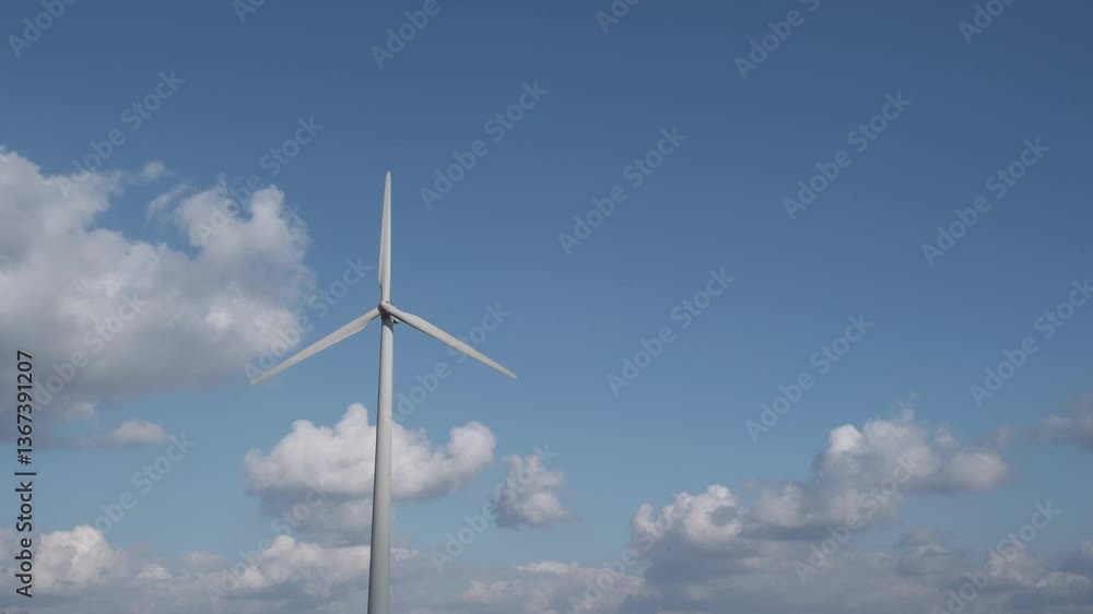 A wind generator rotates against a cloudy blue sky and produces electricity. Green energy concept, which is generated from natural resources such as wind, sun, water. A wind generator rotates against a cloudy blue sky and produces electricity. Green energy concept, which is generated from natural resources such as wind, sun, water.