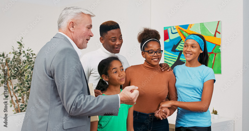 Obraz premium A cheerful family visits an apartment with a real estate agent. The gray-haired man in a suit shows the rooms while the parents and children follow, nodding and smiling with interest.
